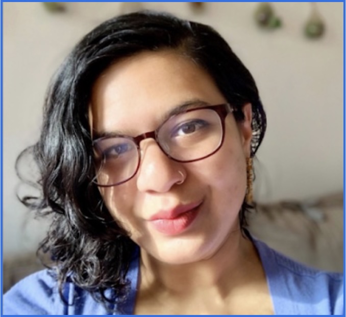 Person with curly dark hair and glasses smiling